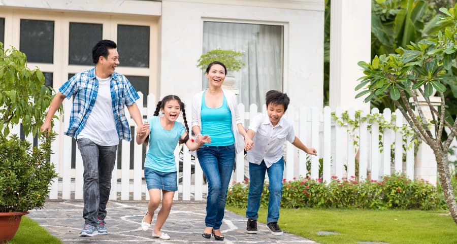 Family members walking hand-in-hand in front of a lovely home with a white fence